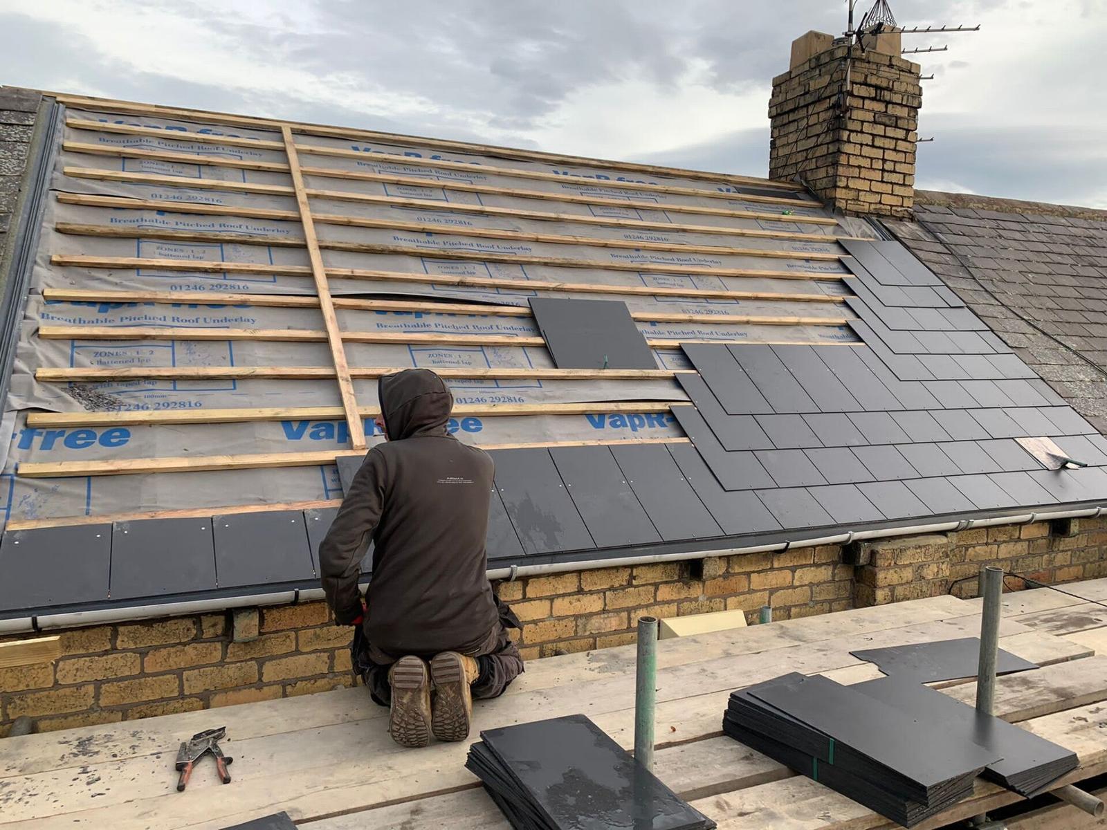 roofer kneeling laying slates at stone gable