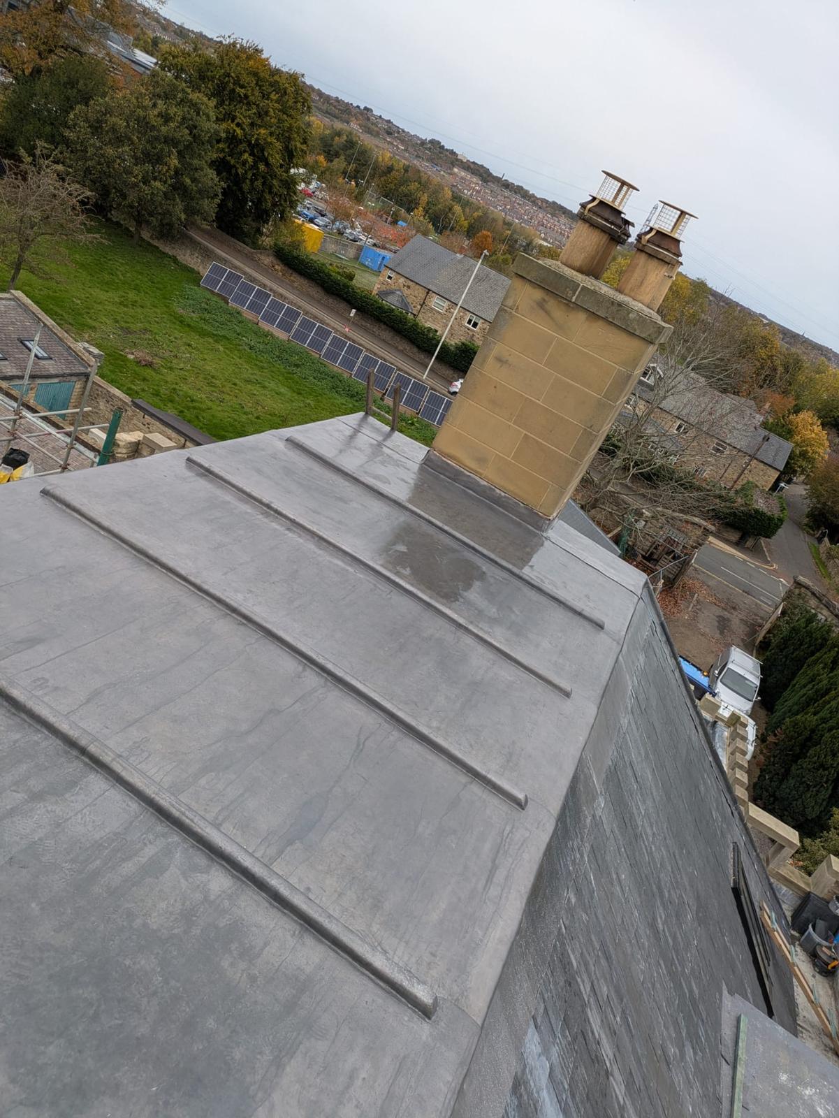 full lead roof with traditional rolls up to a sandstone chimney, village beyond